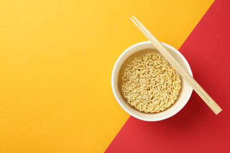 Cup of instant noodles with chopsticks on color background, top view. Space for textの写真素材