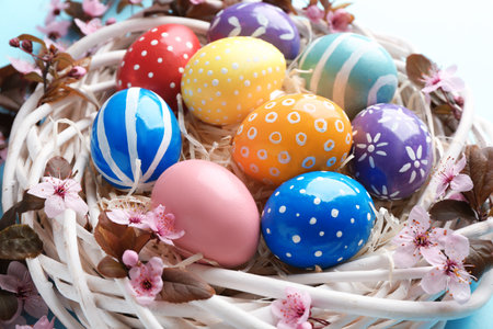 Painted Easter eggs in nest with flowers on color background, closeup