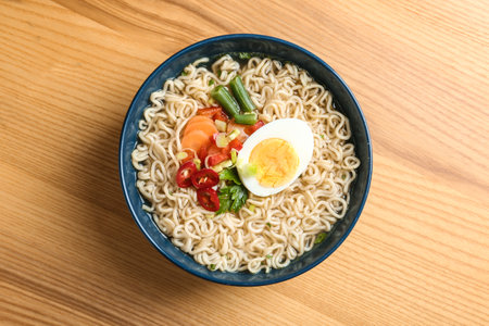 Bowl of noodles with broth, egg and vegetables on wooden background, top viewの写真素材