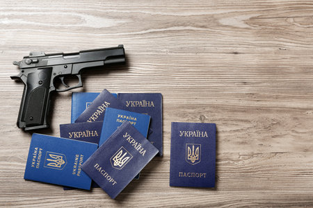 Gun with Ukrainian passports on wooden background, flat lay. Space for text