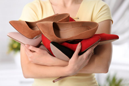 Young woman holding different shoes on blurred background, closeupの写真素材