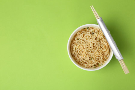 Cup of cooked instant noodles with chopsticks on color background, top view. Space for textの写真素材