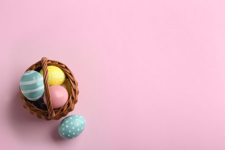 Wicker basket with painted Easter eggs on color background, top view. Space for textの写真素材