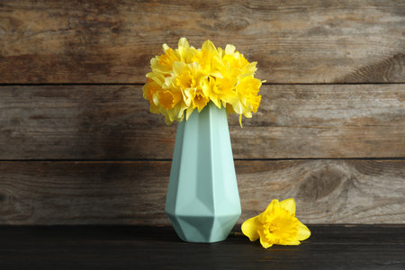 Bouquet of daffodils in vase on table against wooden background. Fresh spring flowersの写真素材