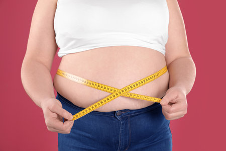 Overweight woman measuring waist with tape on color background, closeupの写真素材