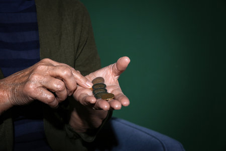Poor senior woman with coins on color background, closeup. Space for textの写真素材