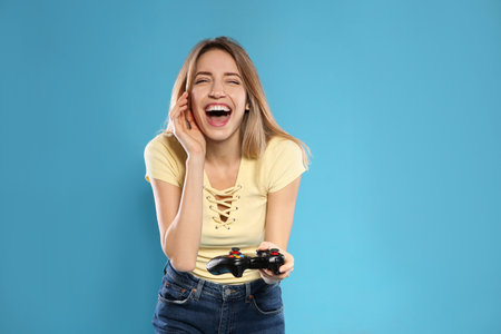 Emotional young woman playing video games with controller on color background. Space for textの写真素材