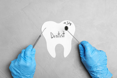 Dentist holding professional tools over paper tooth on gray background, top viewの写真素材