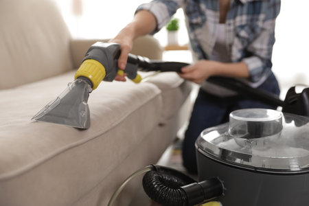 Woman removing dirt from sofa with vacuum cleaner at home, closeupの写真素材