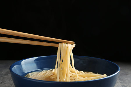 Eating noodle dish with chopsticks against black backgroundの写真素材