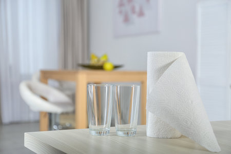 Roll of paper towels and glasses on table indoors. Space for textの写真素材