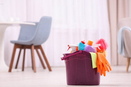 Bucket with cleaning supplies on floor indoors. Space for textの写真素材