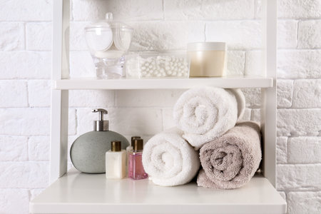 Shelving unit with clean towels and toiletries near brick wallの写真素材