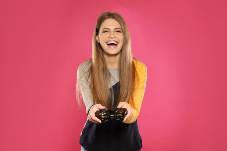 Emotional young woman playing video games with controller on color backgroundの写真素材