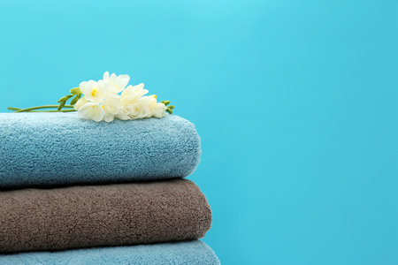 Stack of soft clean towels with beautiful flowers on color background. Space for textの写真素材