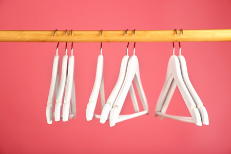 Empty clothes hangers on wooden rail against color backgroundの写真素材