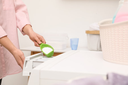 Woman pouring powder into drawer of washing machine in laundry room, closeupの写真素材