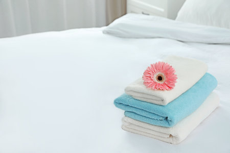 Stack of clean towels with flower on bed indoors. Space for textの写真素材
