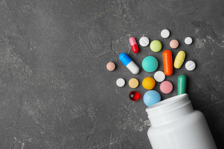 Bottle with different pills on gray background, flat lay. Space for text