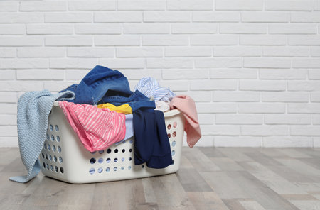 Laundry basket with dirty clothes on floor near brick wall. Space for textの写真素材