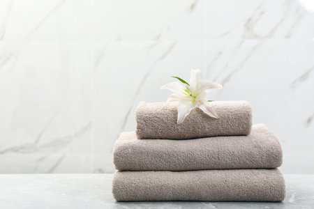 Stack of fresh towels with flower on gray table against light background. Space for textの写真素材