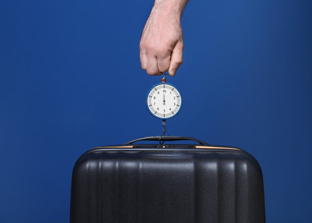 Man weighing stylish suitcase against color background, closeupの写真素材