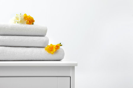 Stack of fresh towels with flowers on cabinet against white background. Space for textの写真素材