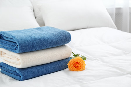 Stack of clean towels and beautiful rose flower on bed. Space for textの写真素材