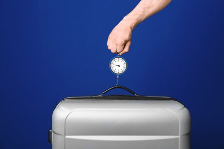 Man weighing stylish suitcase against color background, closeupの写真素材