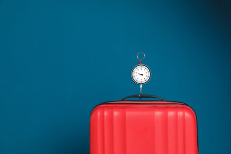 Modern suitcase and hanging scales against color background, space for textの写真素材