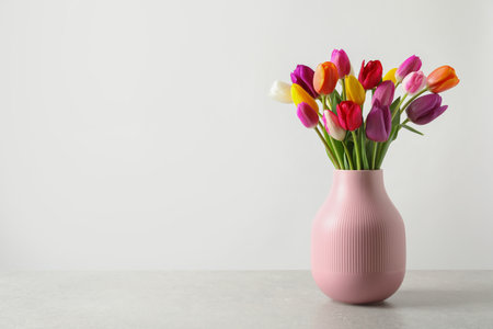 Vase with beautiful spring flowers on table against light background, space for textの写真素材