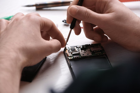 Technician fixing mobile phone at table, closeup. device repair serviceの写真素材