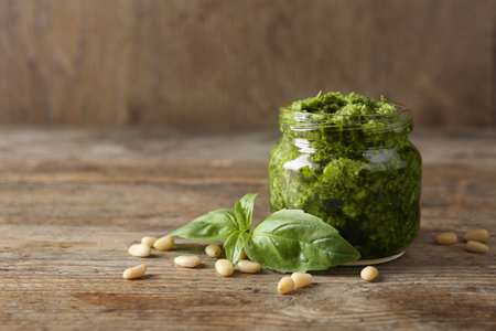 Jar of pesto sauce with basil leaves and pine nuts on wooden table. Space for textの写真素材