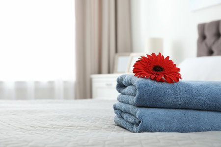 Stack of clean towels with flower on bed indoors. Space for textの写真素材