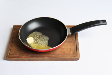 Frying pan with melting butter on board against white backgroundの写真素材