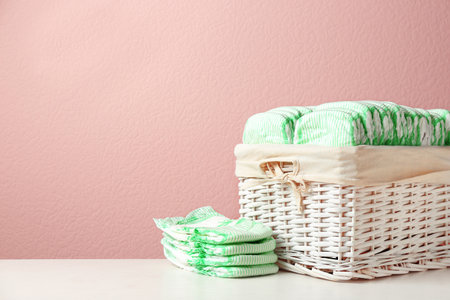 Wicker basket and disposable diapers on table against color background, space for text. baby accessoriesの写真素材