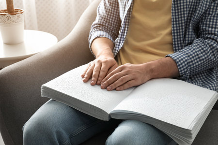Blind man reading book written in Braille on sofa, closeupの写真素材