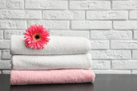 Stack of folded soft towels with flower on table near brick wall. Space for textの写真素材