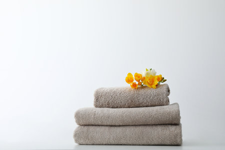 Stack of fresh towels with flowers on table against white backgroundの写真素材