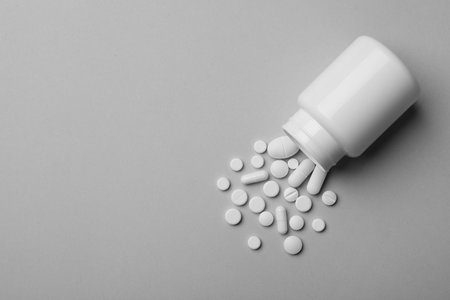 Bottle with different pills on gray background, flat lay. Space for textの写真素材