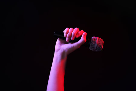 Woman holding microphone on black background, closeupの写真素材