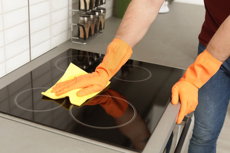 Young man cleaning oven cooktop with rag in kitchen, closeupの写真素材