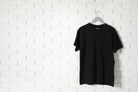 Hanger with black t-shirt against brick wall. Mockup for designの写真素材