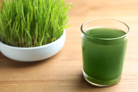Glass of spirulina drink and wheatgrass on wooden table, closeup with space for textの写真素材