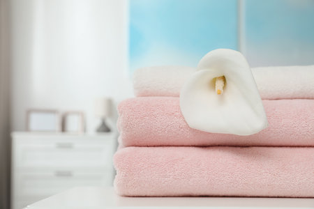 Stack of clean towels with flower on table in room. Space for textの写真素材
