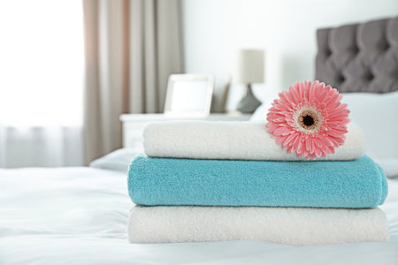 Stack of clean towels with flower on bed indoors. Space for textの写真素材
