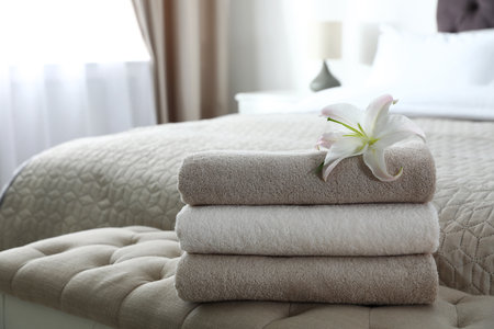 Stack of fresh towels with flower on soft bench in bedroom. Space for textの写真素材