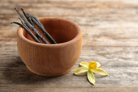 Flower and bowl with vanilla sticks on wooden background. Space for textの写真素材