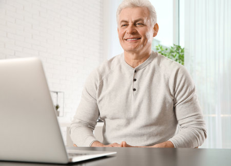 Mature man using video chat on laptop at homeの写真素材