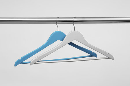 Empty clothes hangers on metal rail against light backgroundの写真素材